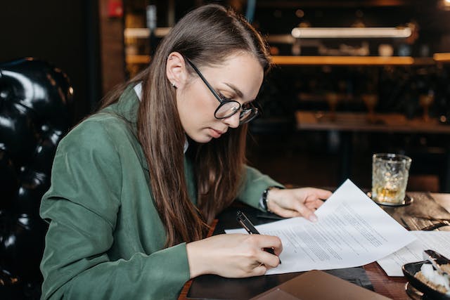 A professional woman in glasses signs on paper that looks like a refinishing warranty document