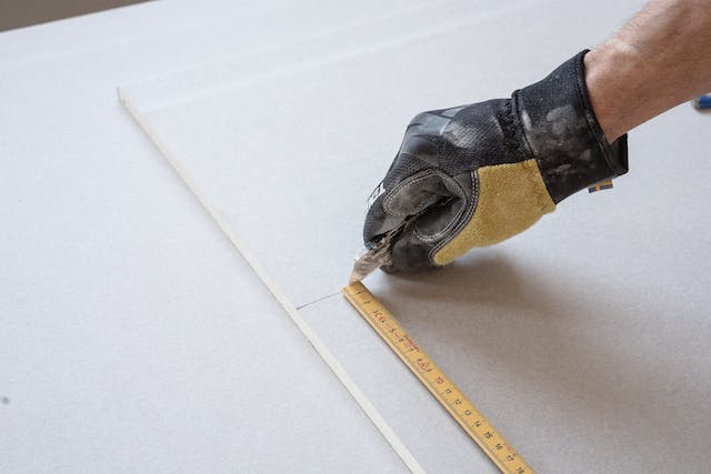 A person measures the length of a wooden plank with a ruler