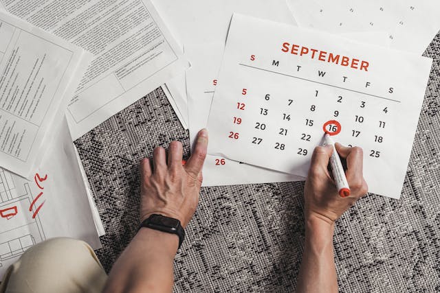 A hand, writing on a calendar with a pen on a table