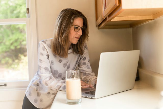 A woman sitting at a kitchen counter, engrossed in using a laptop computer