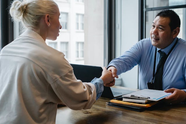 A man and woman shake hands across a desk, symbolizing a professional agreement