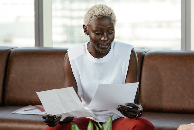 A woman seated on a couch meticulously reading two paper documents