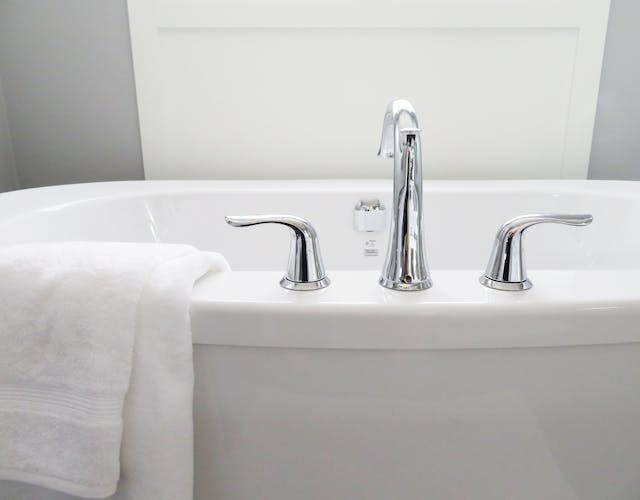 An elegant white bathtub featuring dual faucets and a pristine towel carefully arranged beside it