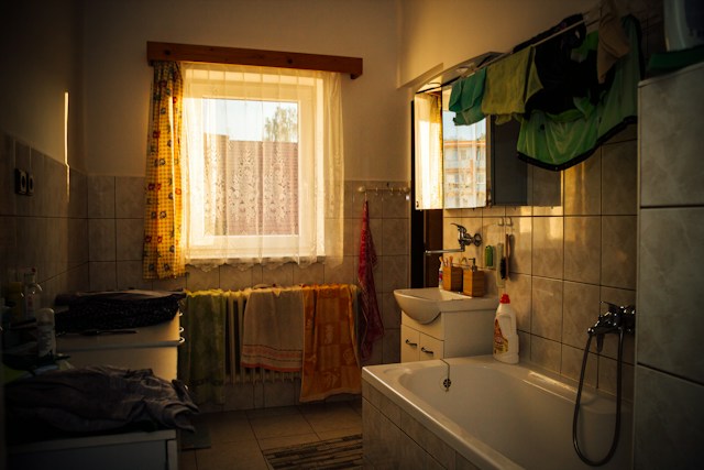 Old and cluttered bathroom with a sink, tub, and window