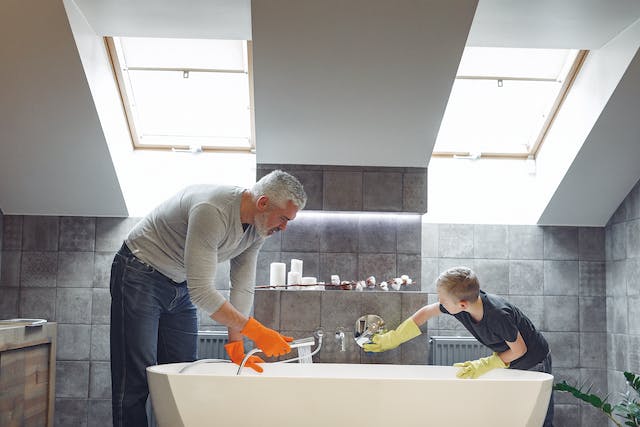 A man and a young boy diligently scrubbing a bathtub, ensuring its cleanliness and hygiene