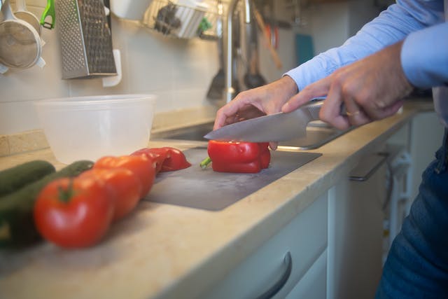 A man prepares peppers by slicing them on a cutting board on a marble countertop
